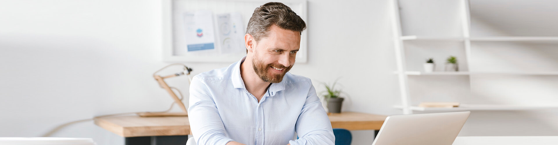 Servicios para tu gestión diaria Empresas - Hombre de negocios con camisa y sonriendo mientras se encuentra trabajando con su portatil en la oficina